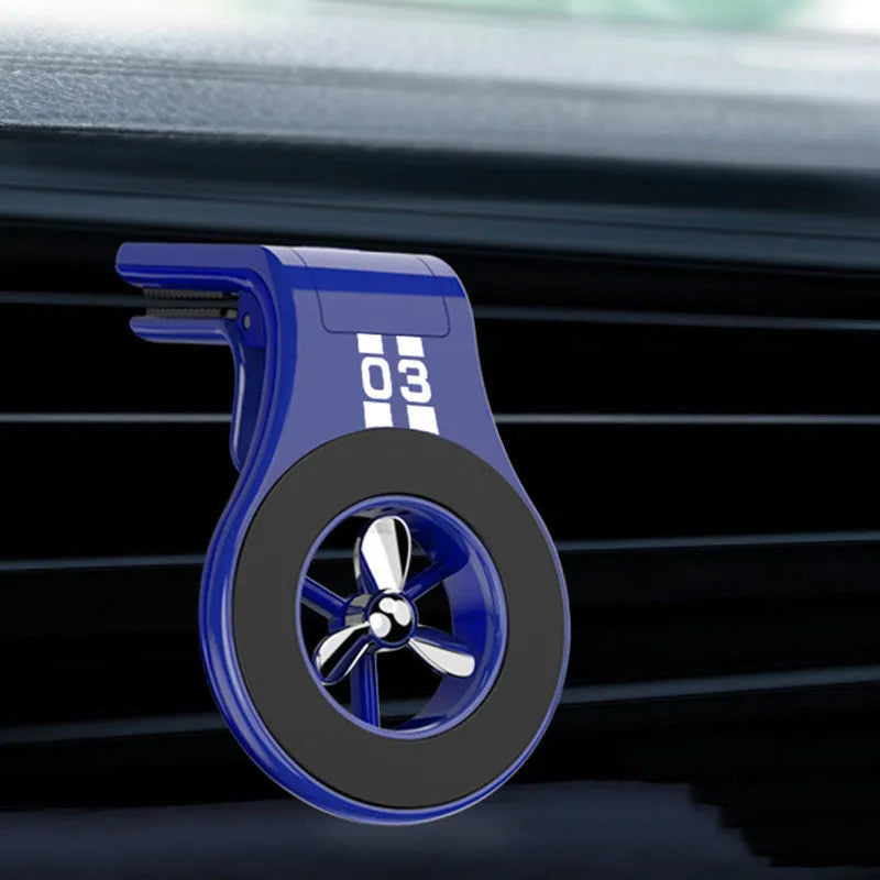 Black magnetic car phone holder clipped to a car air vent, showing adjustable paddle and fragrant slice.