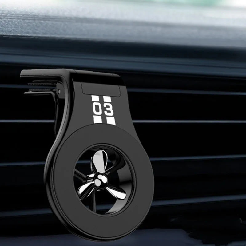 Black magnetic car phone holder clipped to a car air vent, showing adjustable paddle and fragrant slice.