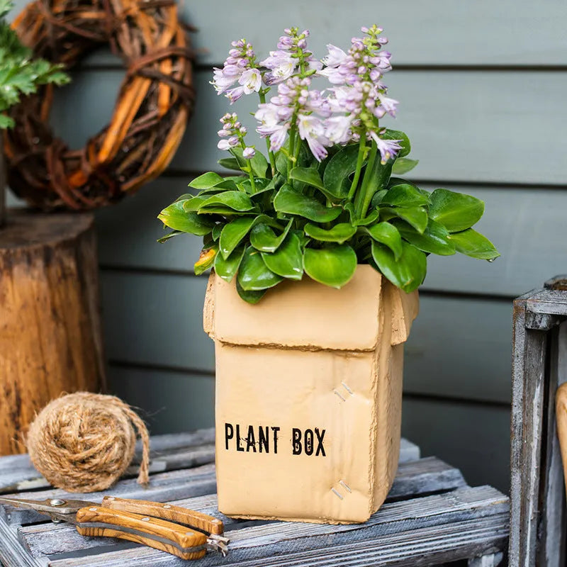 Cement flowerpot with brown paper box design on a floor, showing pre-perforated drainage holes.