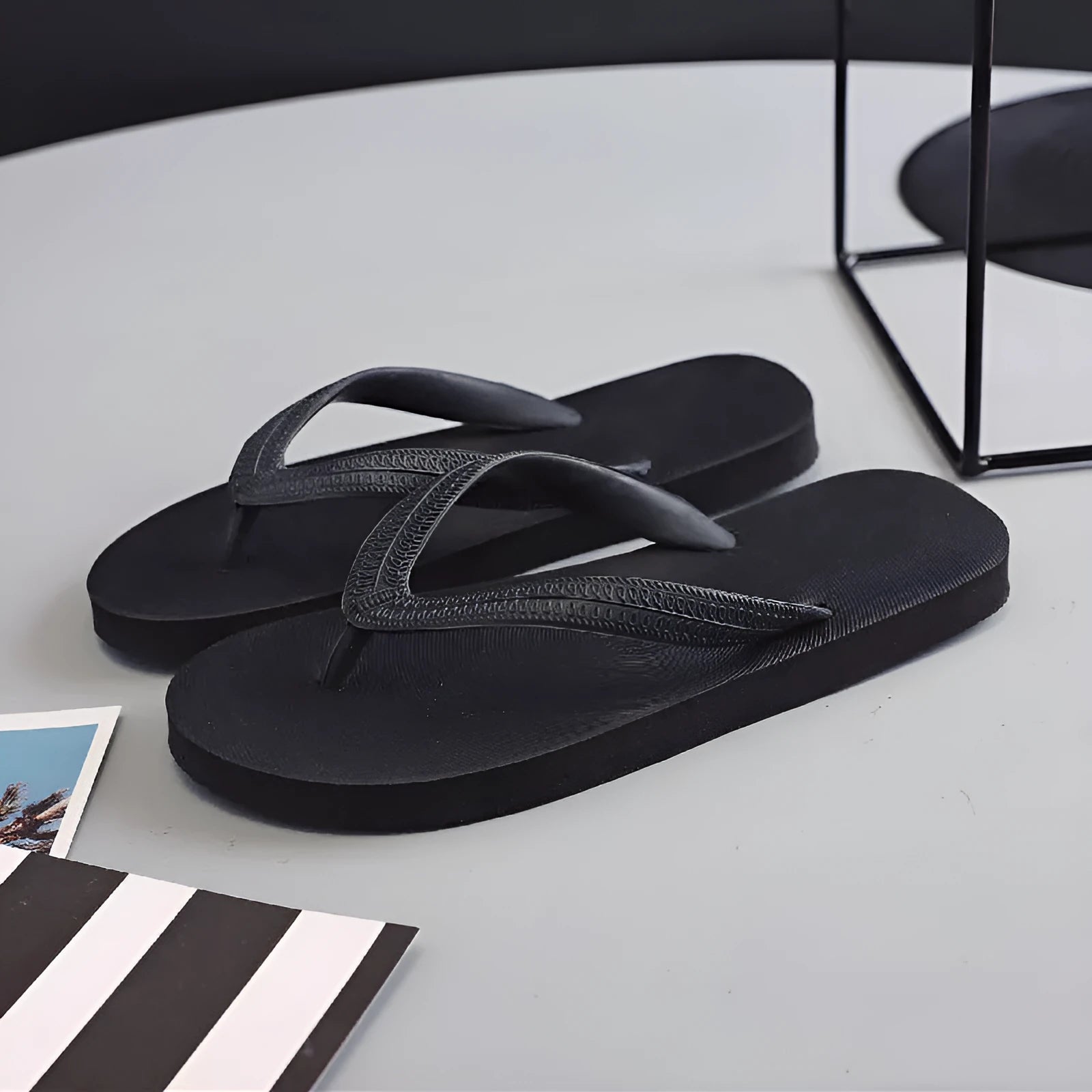 Men's rubber flip-flops in black with a fish logo, showing non-slip sole tread.