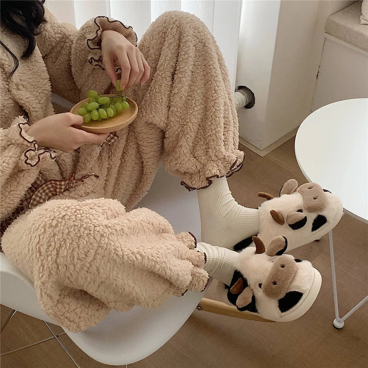 White cartoon cow plush house slippers for women with a non-slip textured sole.