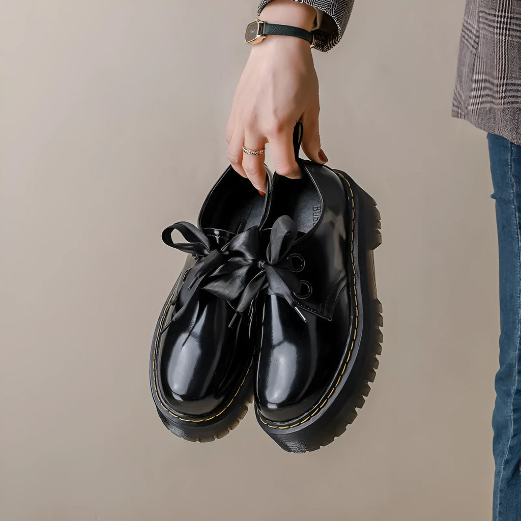 Women's black thick-soled lace-up shoes with ribbon and cross-strap design on a white background.