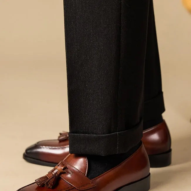 Men's black polished leather tassel loafers with a rubber sole on a white background.
