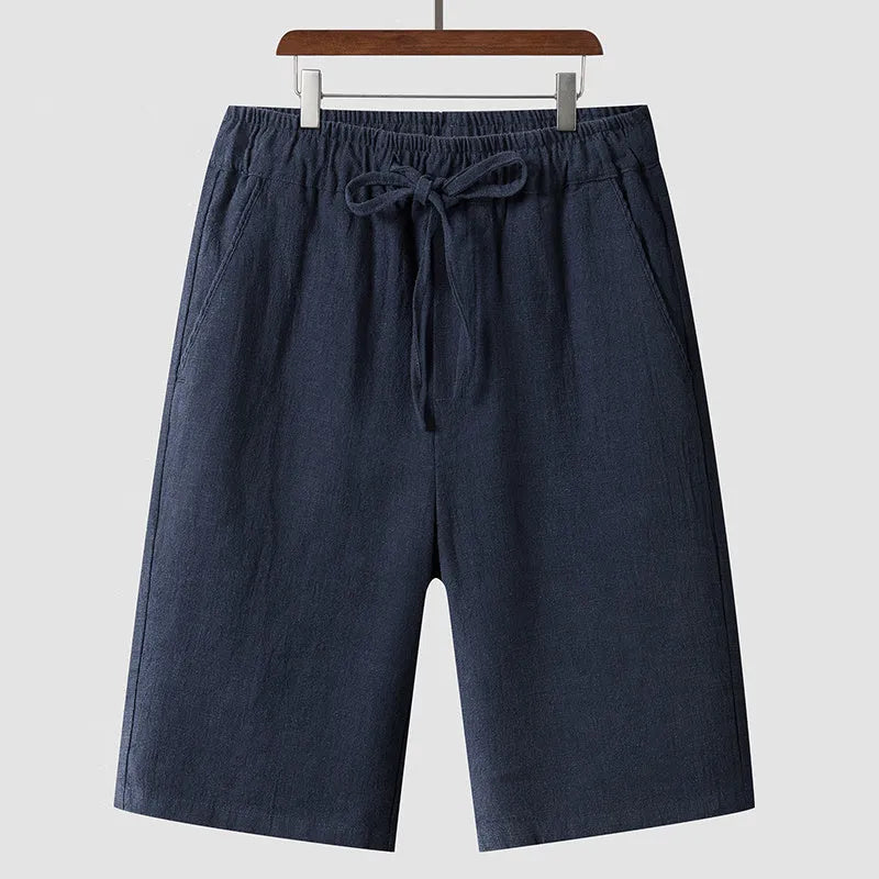 Men's beige linen casual shorts with a loose fit and cropped length on a plain background.
