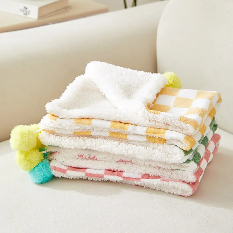 Plush pet blanket with plaid pattern and fur ball decoration on furniture with cat