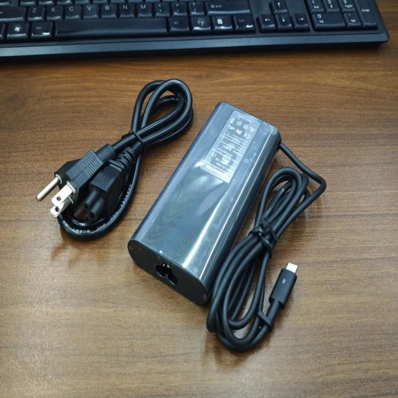 Black 65W USB-C laptop power adapter with a set of international plug cords for UK, US, EU, AU and SA sockets.