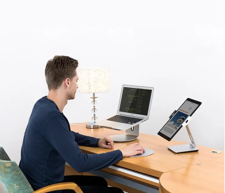Folding aluminium desktop phone and tablet stand with 360-degree rotation on a wooden desk.