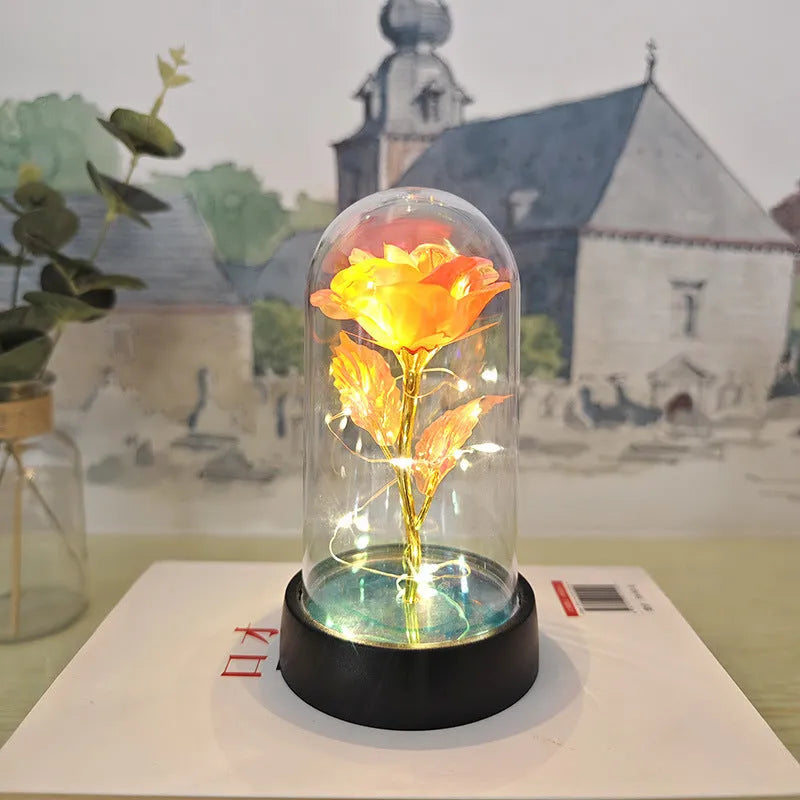 Small decorative table lamp with coloured LED lights illuminating plastic flowers under a glass dome.