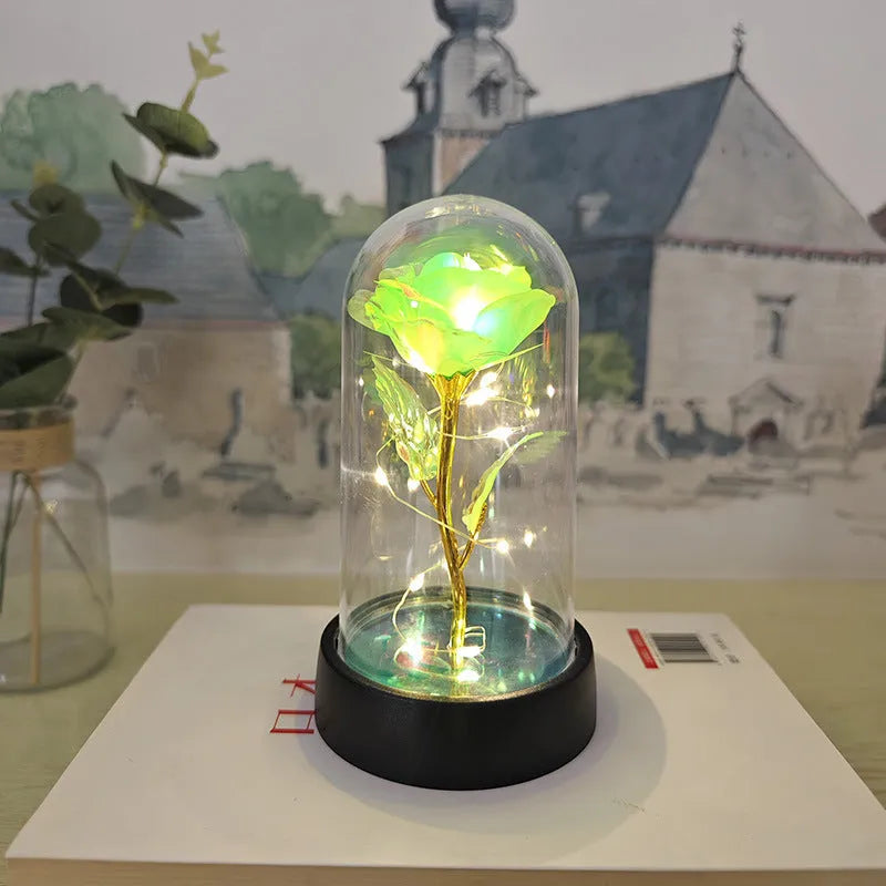 Small decorative table lamp with coloured LED lights illuminating plastic flowers under a glass dome.