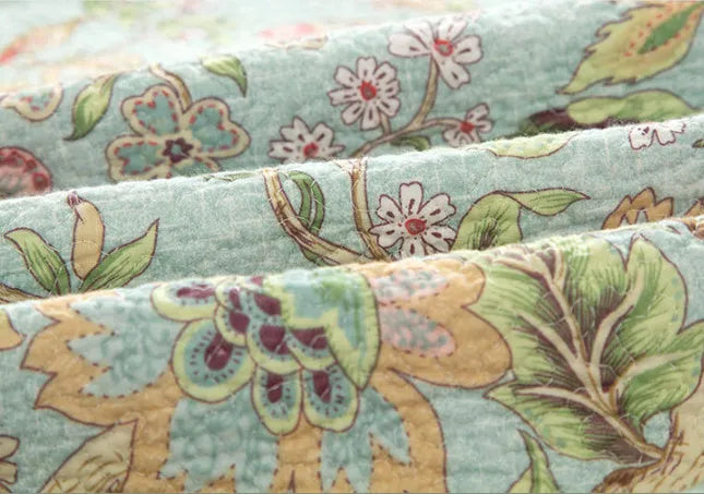Blue cotton quilted bedspread with detailed floral and bird pattern, shown on a bed.