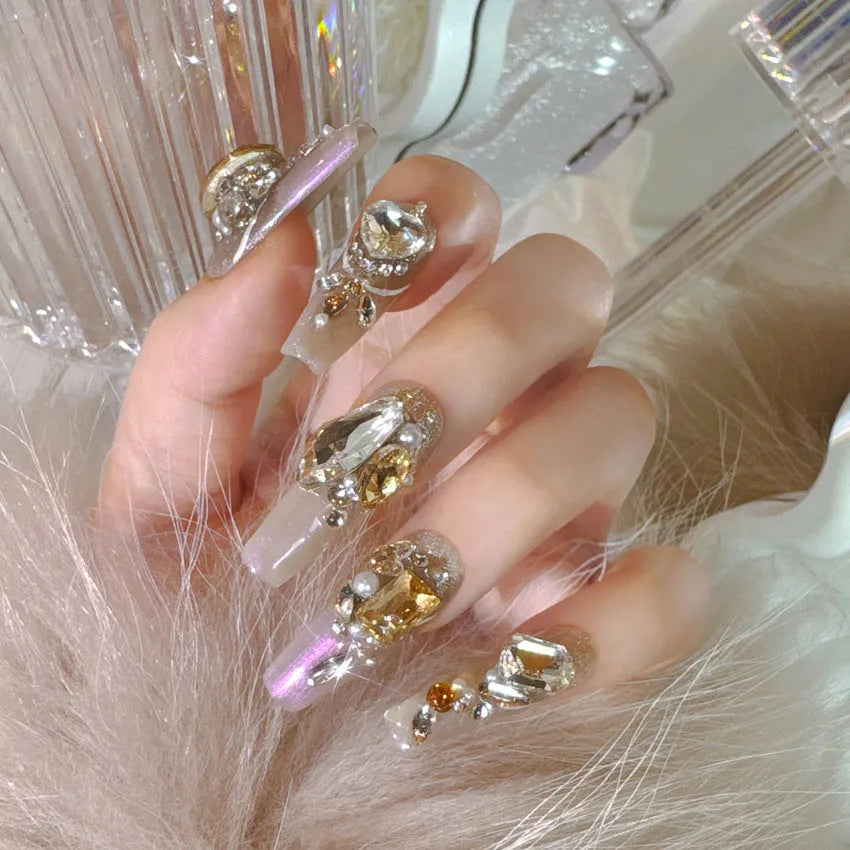 Ten false nail patches with rhinestones on a card, next to jelly adhesive and manicure tools.