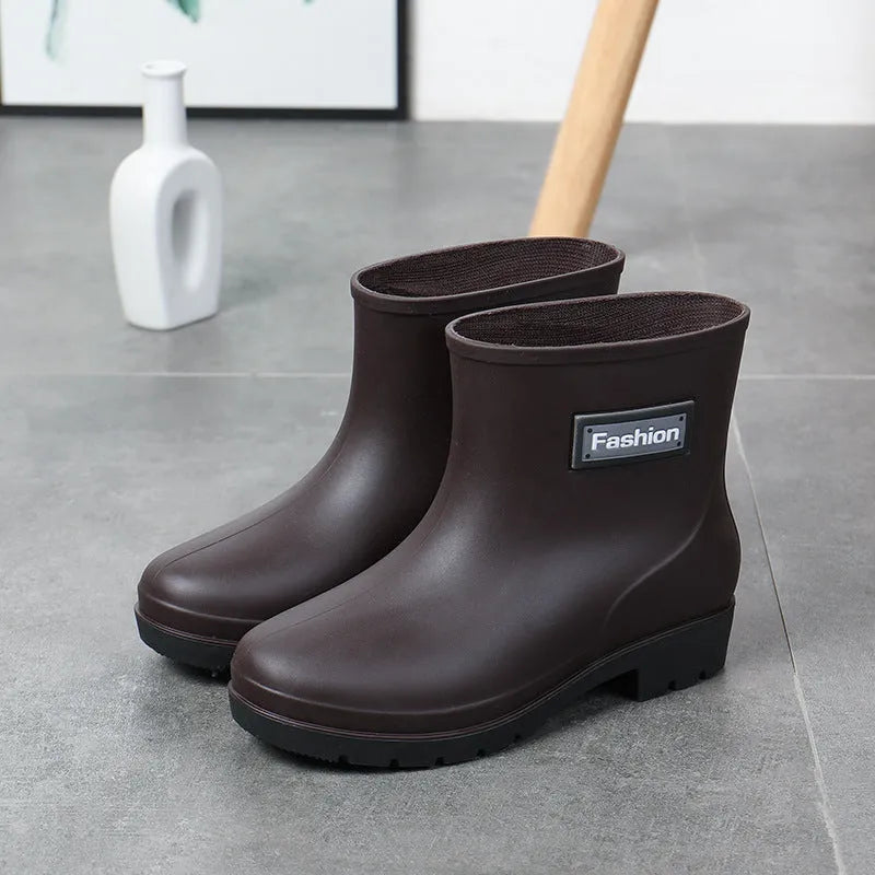 Women's mid-calf PVC rain boot in black on a wet surface, showing low heel and clean design.