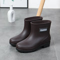 Women's mid-calf PVC rain boot in black on a wet surface, showing low heel and clean design.