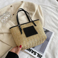 Women's straw woven shoulder bag with PU trim showing tapered shape and sewn thread details