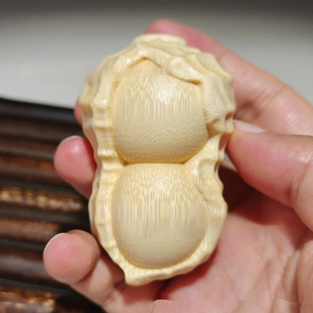 Solid natural bamboo ornament carved into a peanut shape on a plain background.