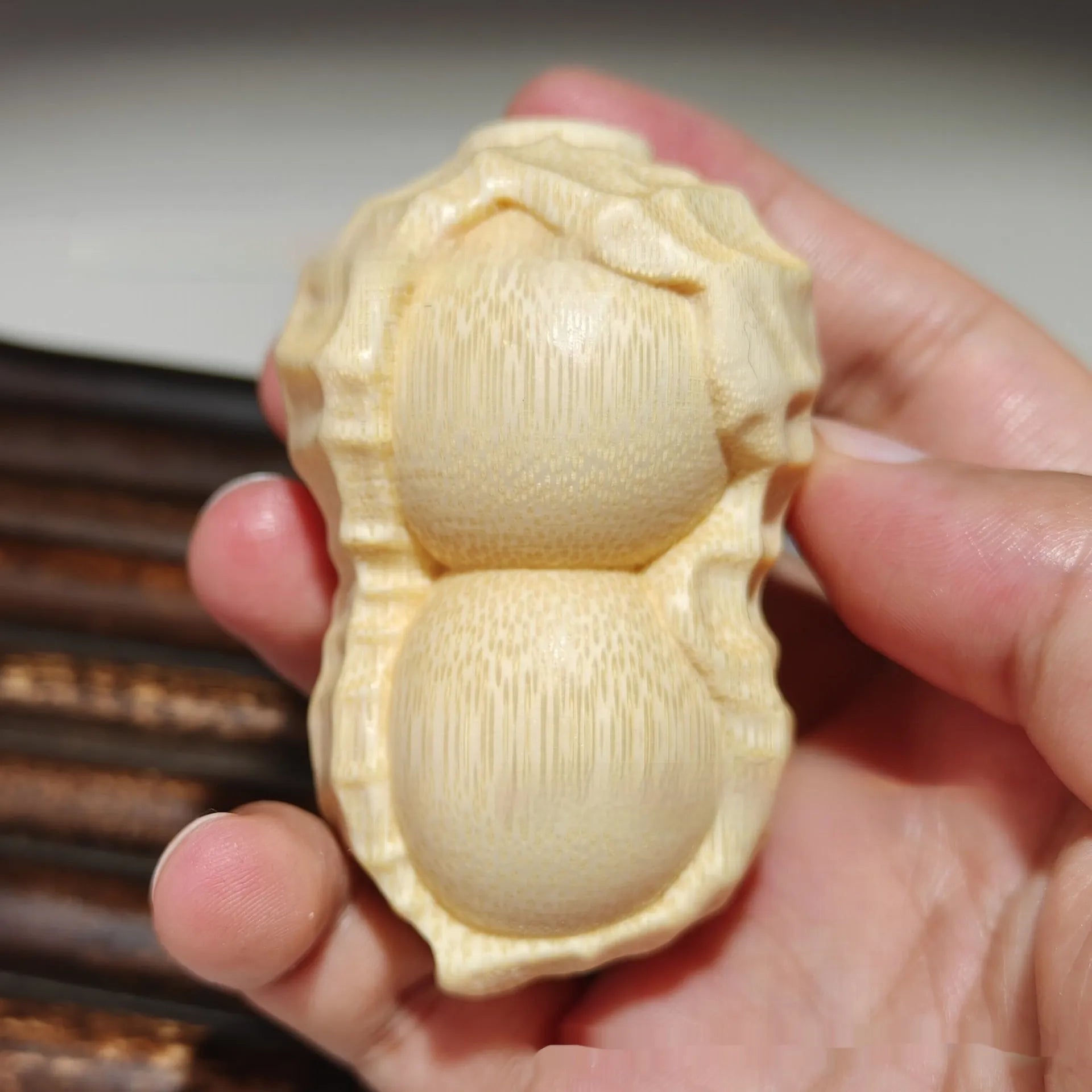 Solid natural bamboo ornament carved into a peanut shape on a plain background.