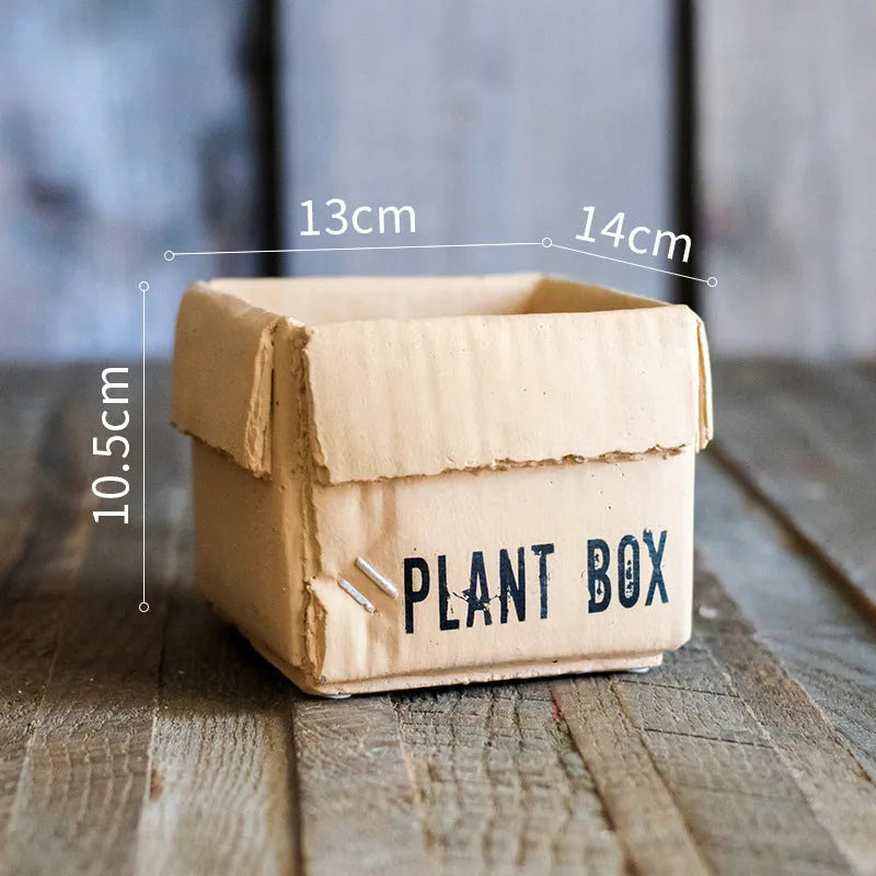 Cement flowerpot with brown paper box design on a floor, showing pre-perforated drainage holes.