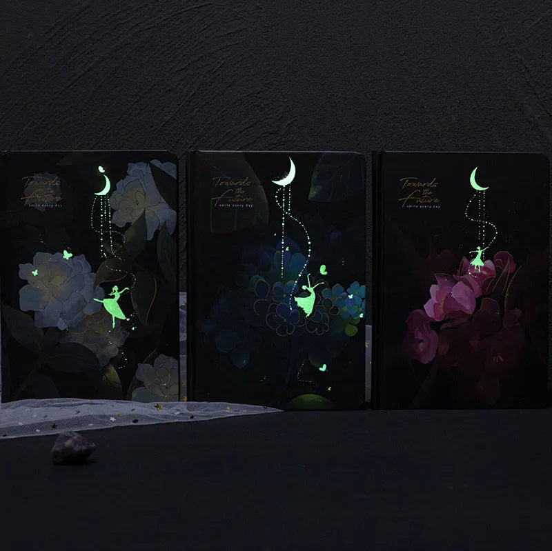 A5 notebook with luminous cover in deep blue, open to show lined pages with colour illustrations.