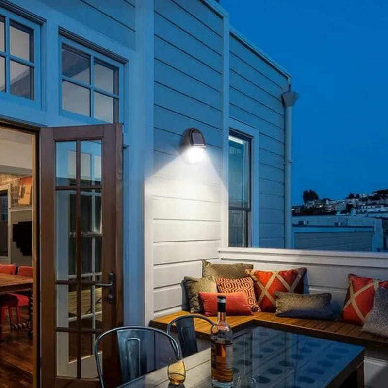 Black rectangular LED solar-powered outdoor wall light mounted on a fence.