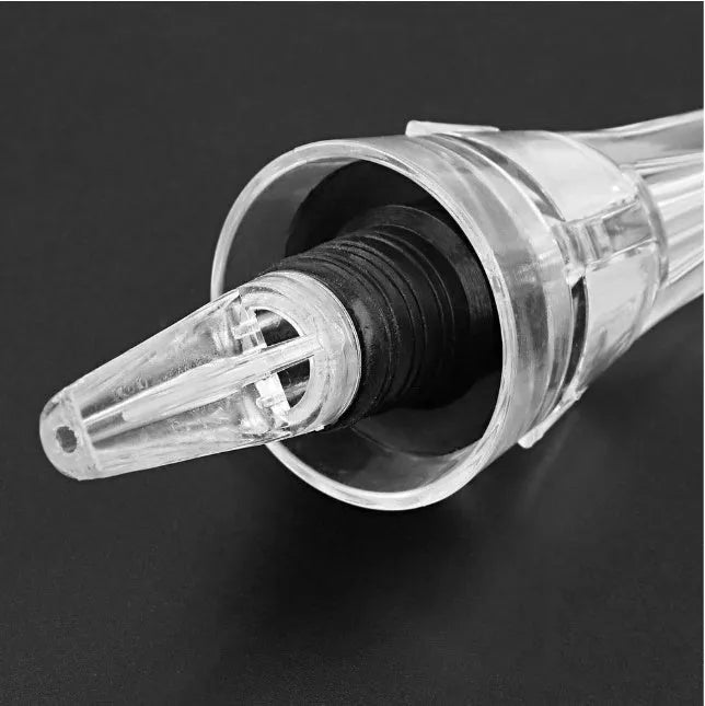 A slender, clear acrylic wine aerator pourer with a stainless steel filter inside, shown next to a wine glass.