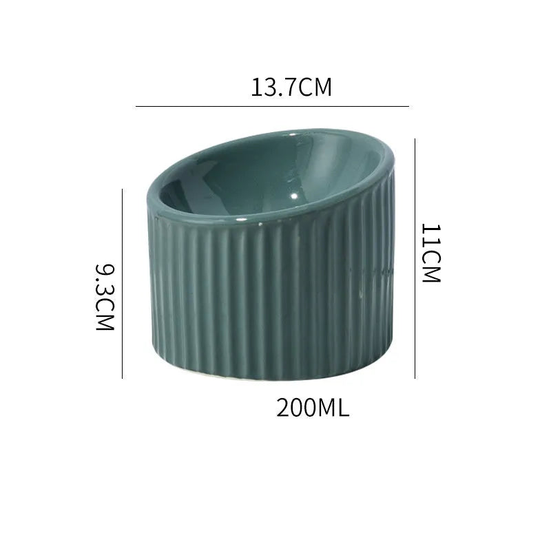 A dark green ceramic elevated cat bowl on a wooden surface, showing its tilted, round shape.
