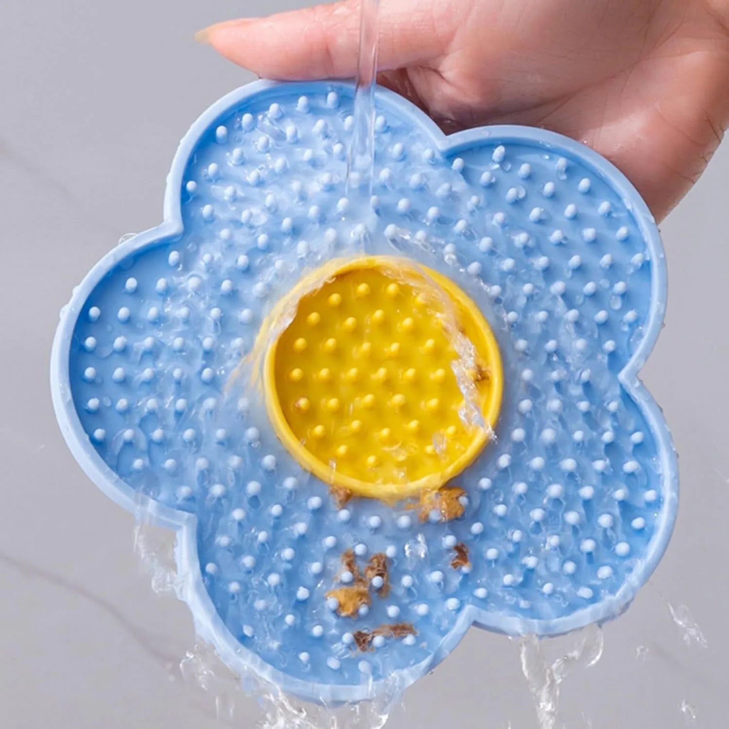 A blue flower-shaped silicone lick mat for pets with four white suction cups on the underside.