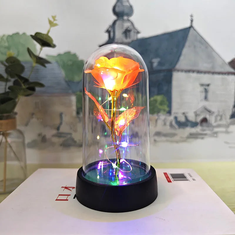 Small decorative table lamp with coloured LED lights illuminating plastic flowers under a glass dome.
