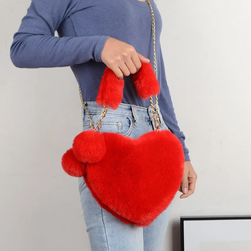 A soft, heart-shaped plush handbag for women in a medium size with a detachable shoulder strap.