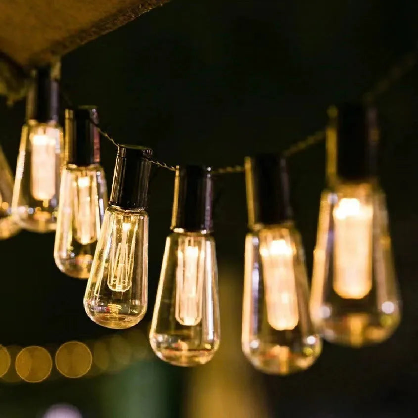 Retro infusion bottle shaped bulb outdoor string lights draped in garden setting