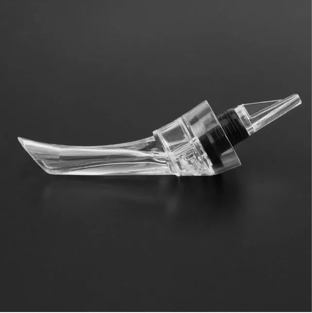 A slender, clear acrylic wine aerator pourer with a stainless steel filter inside, shown next to a wine glass.
