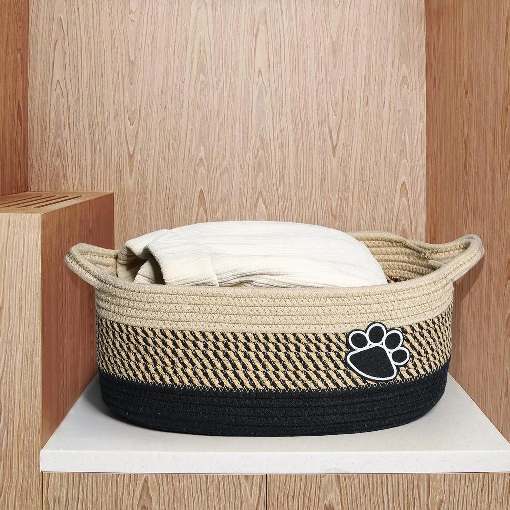 Light beige handmade woven cotton rope storage basket with wooden base and handle on a table.