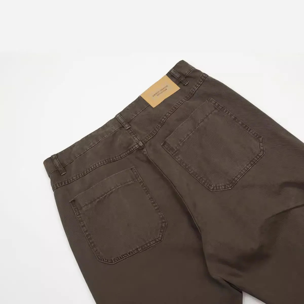 Men's brown loose straight leg high waist cotton trousers laid flat.