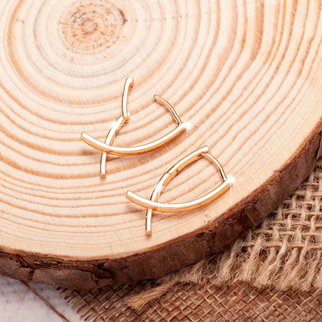 A pair of rose gold coloured cross shaped earrings on a plain background.