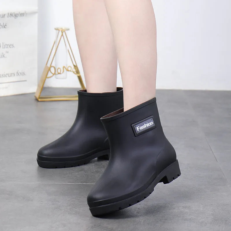 Women's mid-calf PVC rain boot in black on a wet surface, showing low heel and clean design.