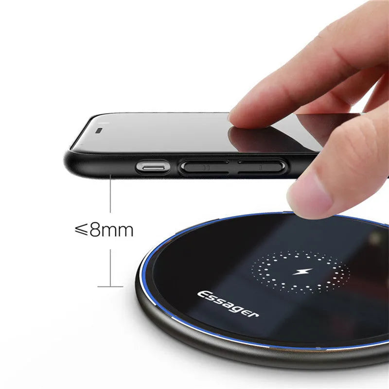 Black 15W fast wireless charging pad on a wooden desk next to a smartphone.