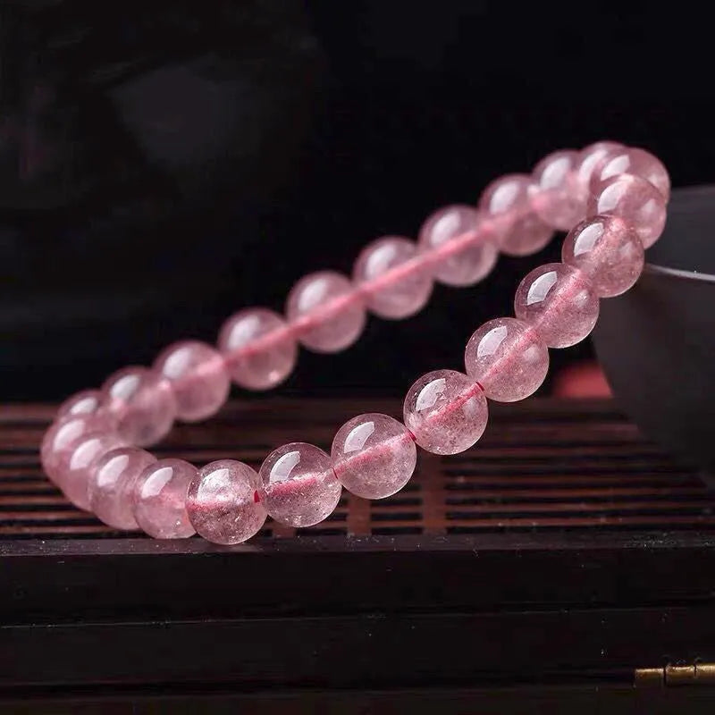 Women's strawberry quartz crystal bracelet with polished round beads on a white background.