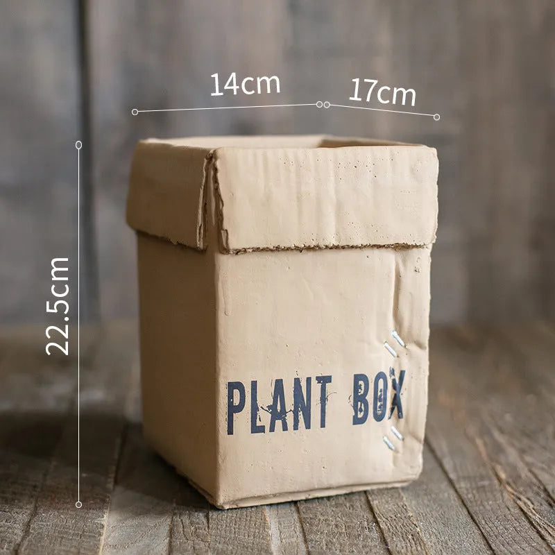 Cement flowerpot with brown paper box design on a floor, showing pre-perforated drainage holes.