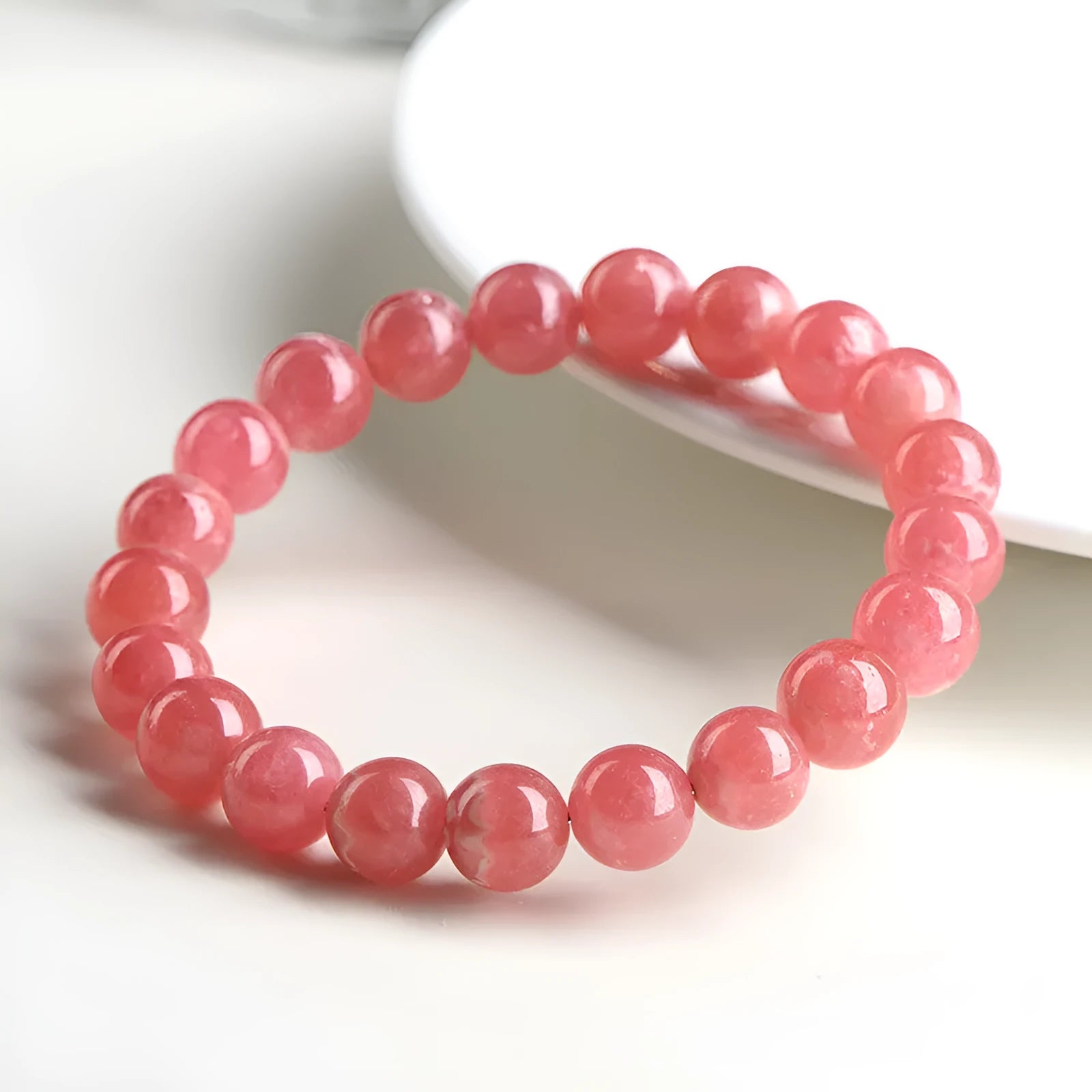 Women's geometric rhodochrosite crystal bracelet with a longevity lock charm on a wrist.