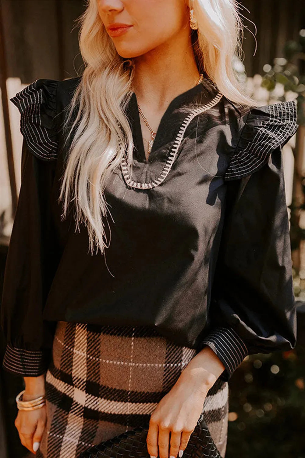 Black V-neck blouse with long ruffle sleeves and white contrast stitching.