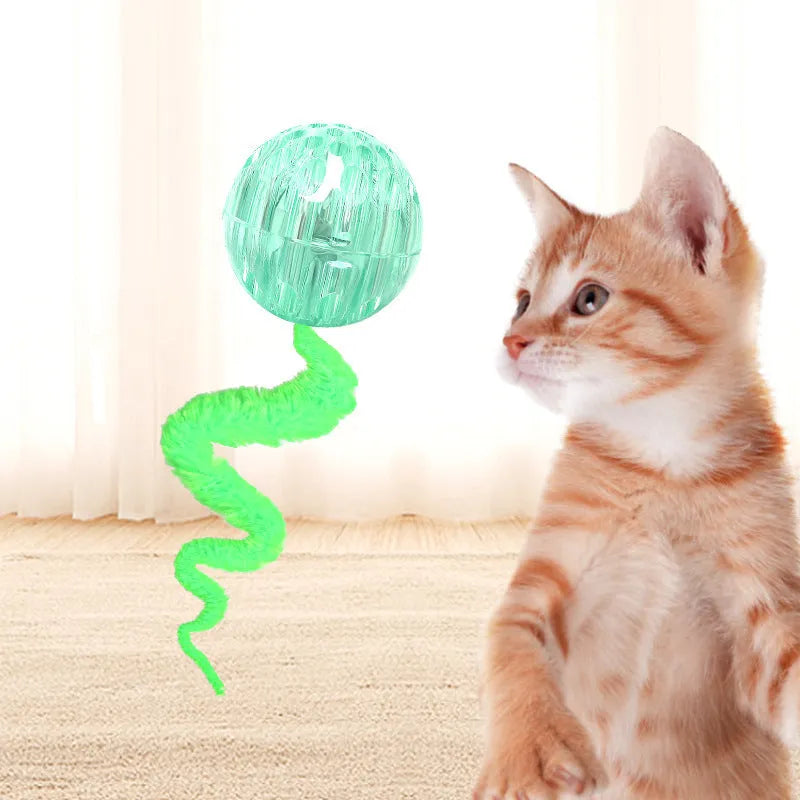 Green TPR bouncy ball with pink plush worm tail cat toy on floor