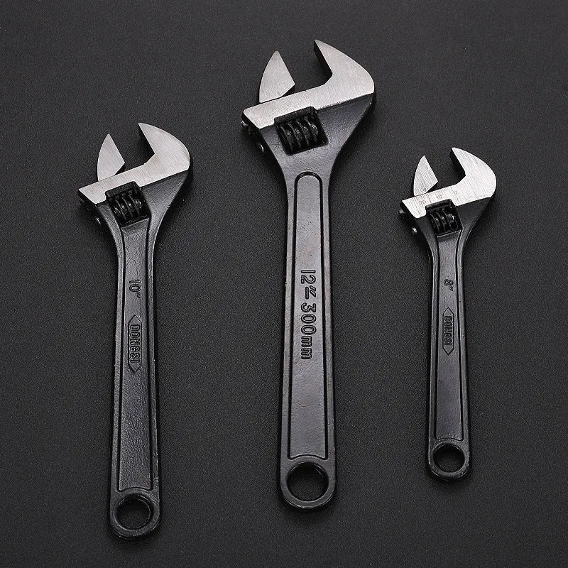 Blackened high-carbon steel adjustable open-end wrench with ergonomic handle on a workbench.