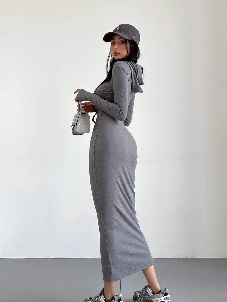 A woman wearing a light grey hooded sheath dress with long sleeves, showcasing the high waist and over-the-knee length.