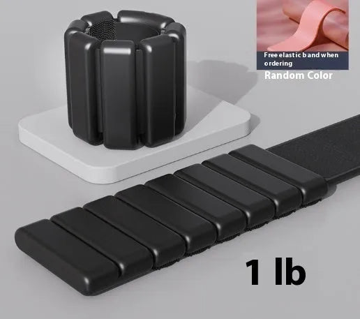 Adjustable black silicone wrist weight bracelet with a detached 2lb metallic weight on a grey background.