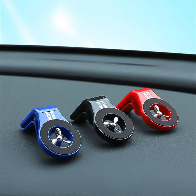 Black magnetic car phone holder clipped to a car air vent, showing adjustable paddle and fragrant slice.