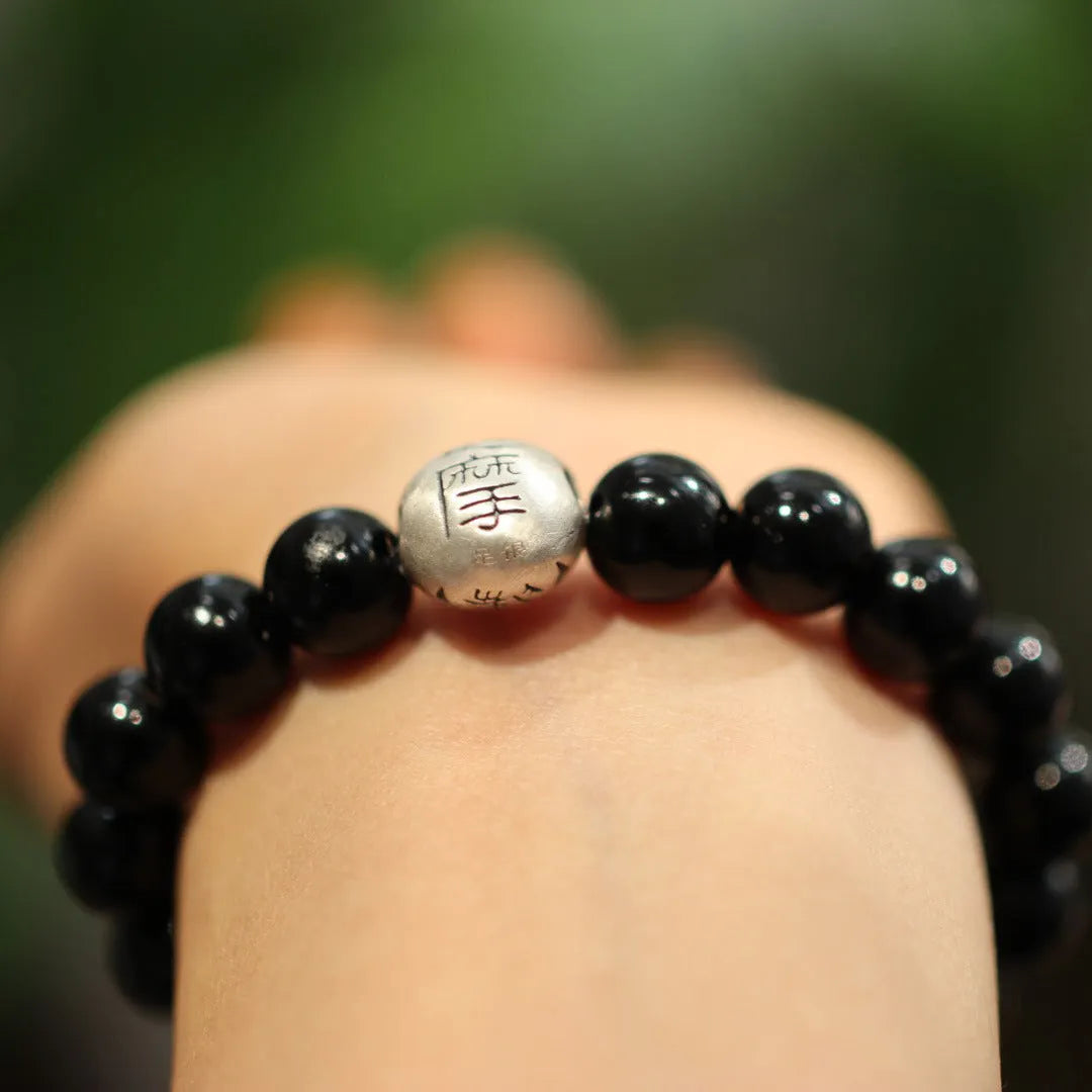 Close-up of a women's bracelet with spherical black agate beads and a shiny sterling silver clasp on a wrist.