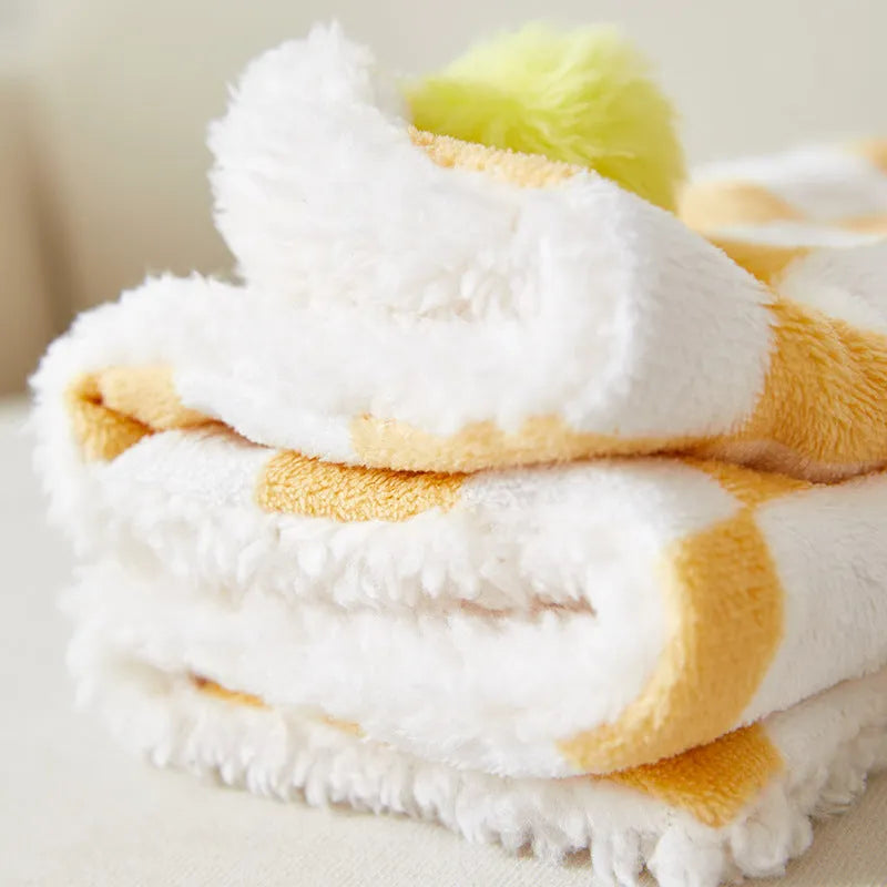 Plush pet blanket with plaid pattern and fur ball decoration on furniture with cat