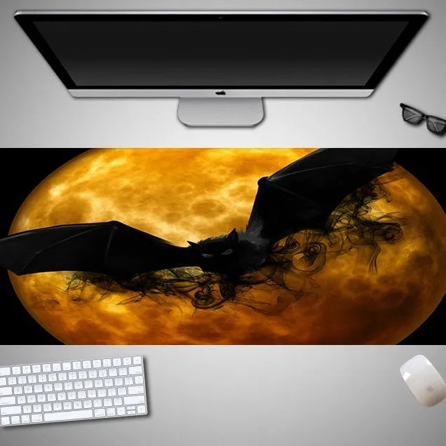 Oversized black Halloween-themed mouse pad with spooky artwork on a desk next to a gaming mouse.
