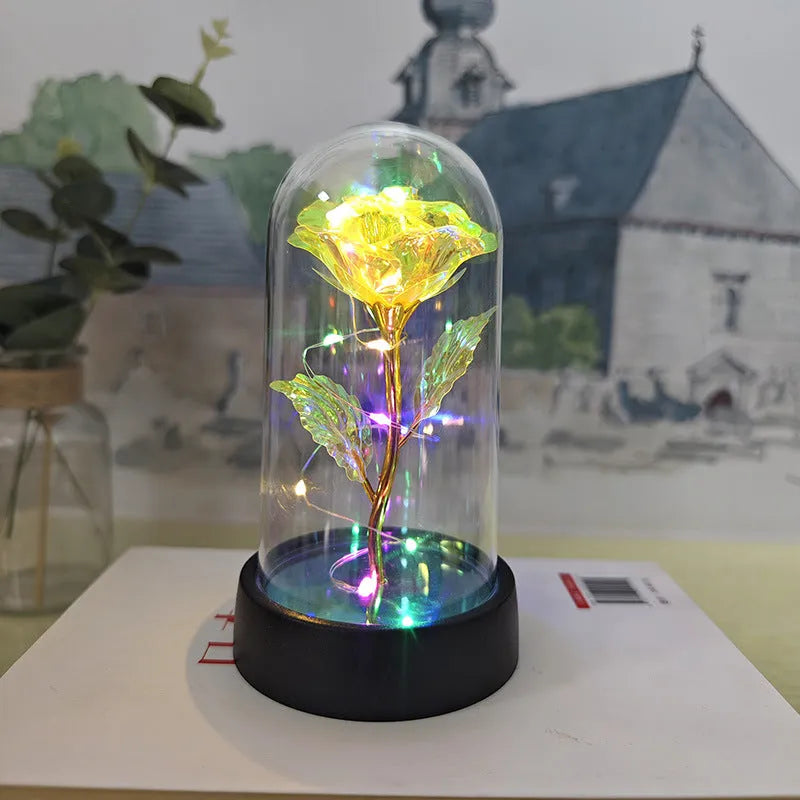 Small decorative table lamp with coloured LED lights illuminating plastic flowers under a glass dome.