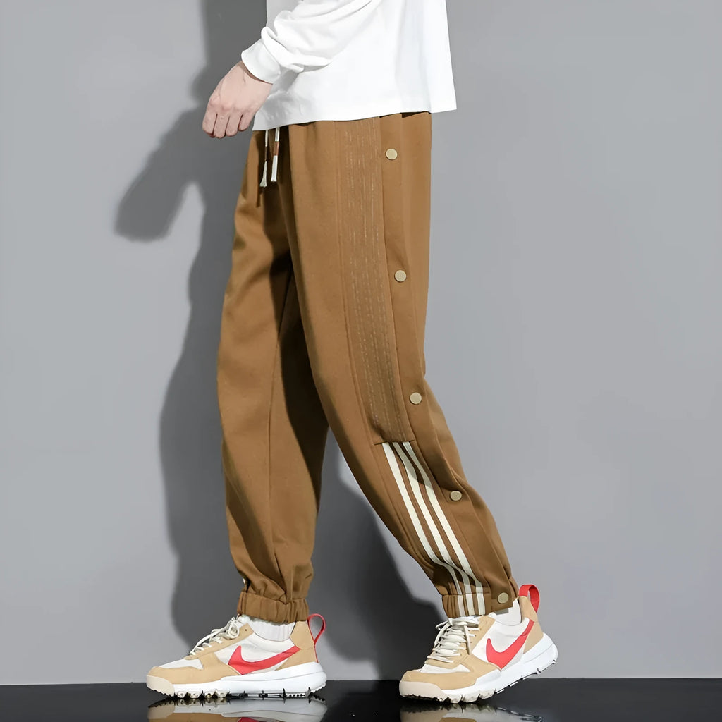 Men's black high-waist sweatpants with ankle-tied cuffs and a drawstring waist on a grey background.