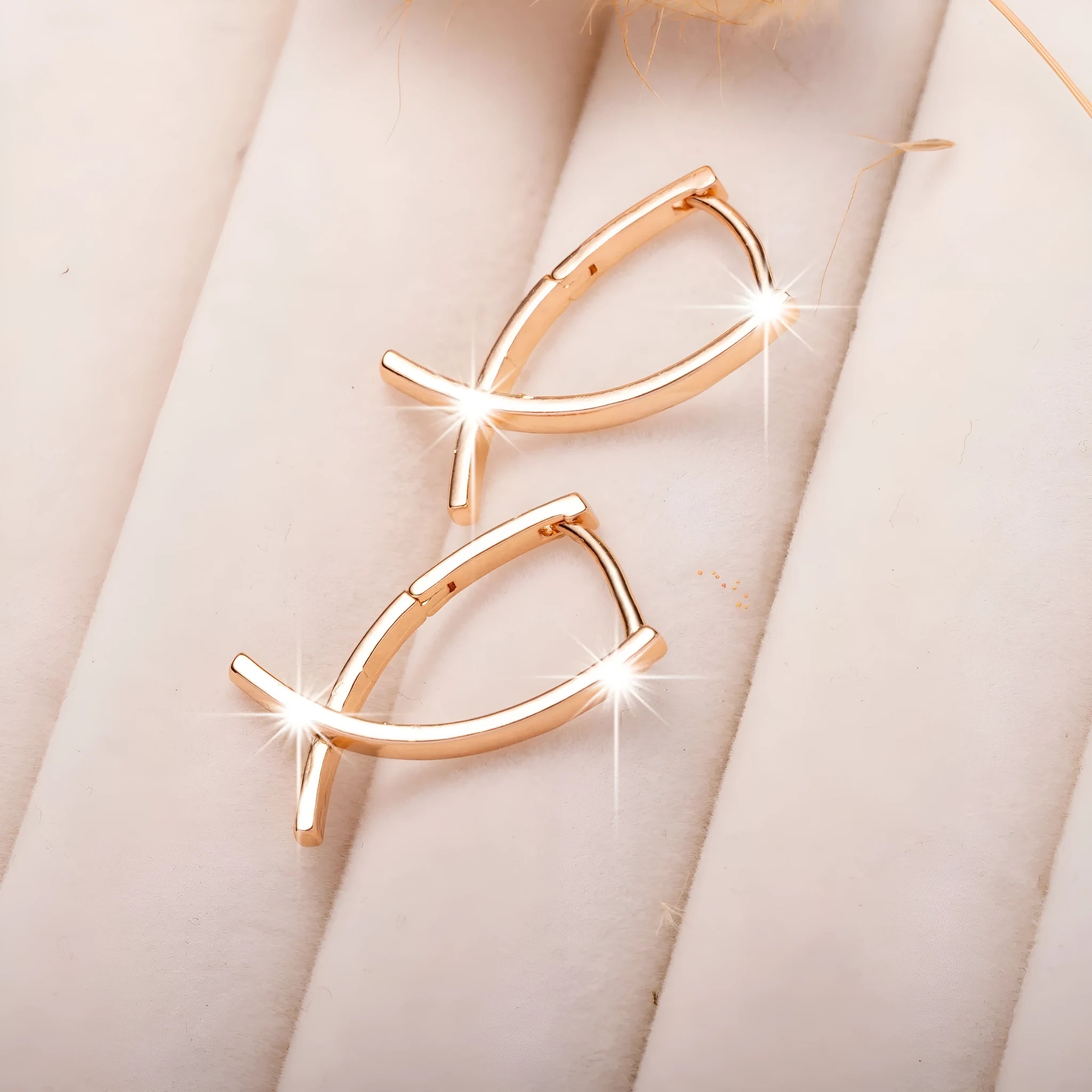 A pair of rose gold coloured cross shaped earrings on a plain background.